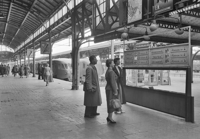 155113 Afbeelding van enkele reizigers bij een vertrektijdenbord op het perron van het N.S.-station Groningen te Groningen.